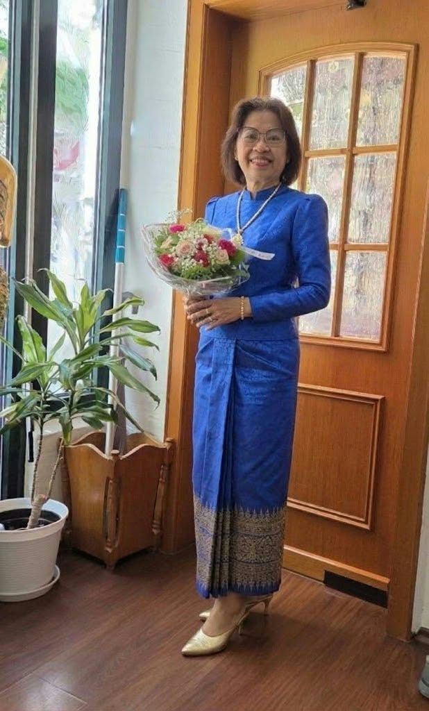 Mitarbeiterin von YADA in einem königsblauen thailändischen Kleid mit Blumen am Eingang